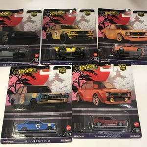Peut inclure: Un ensemble de dix voitures miniatures Hot Wheels, chacune représentant un modèle de voiture japonais différent. Les voitures sont présentées sur leur emballage individuel, qui arbore un design d'inspiration japonaise avec des fleurs de cerisier et un soleil rouge. Les voitures sont toutes de couleurs différentes, notamment rouge, bleu, jaune et orange.
