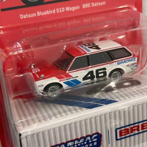 Op de afbeelding: Een rood, wit en blauw Datsun Bluebird 510 Wagon speelgoedauto met nummer 46. De auto zit in een transparante plastic verpakking met de tekst "Tarmac Works" en "BRE Datsun". Een gedetailleerde miniatuur.
