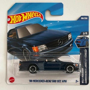 May include: A blue Hot Wheels die-cast toy car of a '89 Mercedes-Benz 560 SEC AMG. The car is in a clear plastic package with a blue and white background. The package includes the Hot Wheels logo and the text "WILD WIDEBODY".