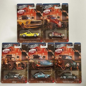 May include: A collection of Hot Wheels die-cast model cars on their original packaging. The cars include a yellow Mustang, a red roadster, a black hot rod, a blue Porsche, and a green Volkswagen Beetle. Each package features a barn scene.