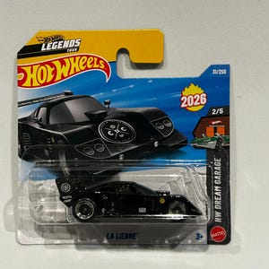 May include: A black Hot Wheels die-cast toy car, "La Liebre", packaged on a blue and yellow card. The card features the Hot Wheels Legends Tour logo and the text "HW Dream Garage". The car is a sleek, black design.
