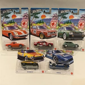 May include: Five Hot Wheels die-cast cars in their packaging. The cars are all Japanese imports and include a red Mazda RX-7, a green Toyota Starlet, a red Nissan Skyline GT-R, a yellow Honda CR-X, and a blue Acura NSX. The packaging features a Japanese mountain scene with cherry blossoms.