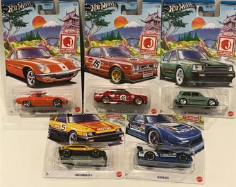 May include: Five Hot Wheels die-cast cars in their packaging. The cars are all Japanese imports and include a red Mazda RX-7, a green Toyota Starlet, a red Nissan Skyline GT-R, a yellow Honda CR-X, and a blue Acura NSX. The packaging features a Japanese mountain scene with cherry blossoms.