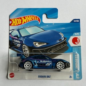 May include: A blue Subaru BRZ Hot Wheels toy car in a plastic package. The car has a white and pink racing stripe and the number 2 on the side. The package has the Hot Wheels logo and the words "Subaru BRZ" on the front.