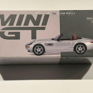 May include: Silver BMW Z8 convertible model car in a box. The box has the words "MINI GT" in large grey letters. The car has a red interior and is a miniature replica.