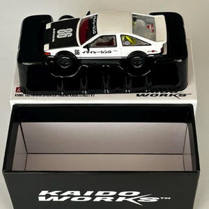 May include: A white and black toy car with the number 86 on the side and top. The car is in a black display case with the text "KAIDO WORKS" on the box. The car has the text "ADVAN" and Japanese text.