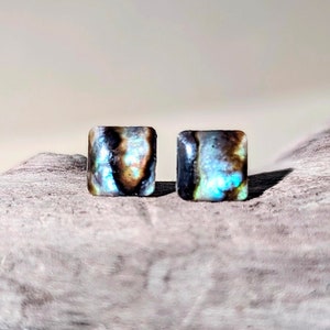 Könnte beinhalten: Ein Paar quadratische Ohrringe mit einem blauen, braunen und weißen irisierenden Muster.