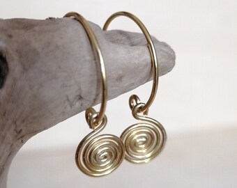 May include: A pair of gold spiral earrings. The earrings are made of wire and are shaped like a spiral. They are hanging from a piece of driftwood.