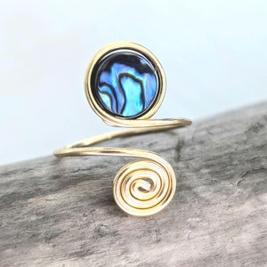 Könnte beinhalten: Ein goldener Drahtring mit einer Einlage aus blauer und schwarzer Abalone-Schale. Der Ring ist spiralförmig gewickelt.
