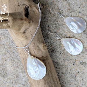 Könnte beinhalten: Ein Schmuckset bestehend aus einer Halskette und einem Paar Ohrringen, jeweils mit einem tropfenförmigen Anhänger aus weißem Perlmutt. Die Halskette hat eine silberfarbene Schlangenkette und die Ohrringe verfügen über silberfarbene Haken.