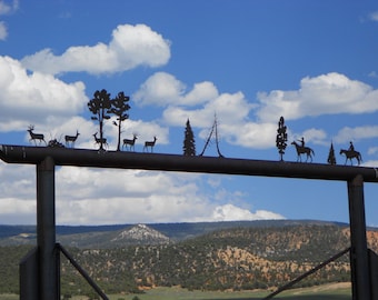May include: A black metal gate topper featuring a silhouette design of a forest scene with deer, pine trees, and two figures riding horses. The metal cutout is mounted horizontally across the top bar of a dark metal gate structure.
