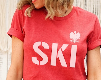Puede incluir: Camiseta roja con un gráfico "SKI" rosa y un diseño de águila blanca.