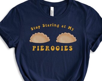 May include: A navy blue t-shirt with the text "Stop Staring at My Pierogies" in yellow. Two cartoon pierogies are above the text.