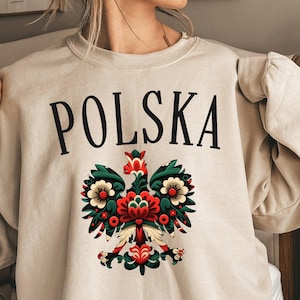 May include: A beige sweatshirt with the word "POLSKA" printed in black on the front. A colorful embroidered eagle with floral designs is below the text.