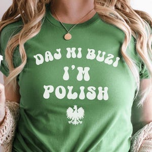 May include: Green t-shirt with white text that reads "DAJ MI BUZI I'M POLISH" and a white graphic of the Polish coat of arms.