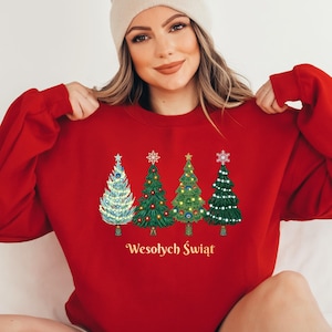 May include: A red long-sleeve sweatshirt featuring a graphic print of four distinct stylized Christmas trees in shades of green, blue, and white, topped with stars and snowflakes. Below the trees, the text Wesołych Świąt is printed in gold.