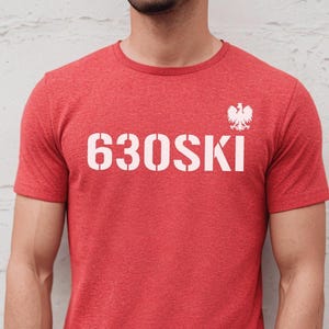 May include: Red t-shirt with the white text "630SKI" in a stencil font. Above the text is a white Polish eagle emblem. The shirt is short-sleeved and made of a heathered fabric.