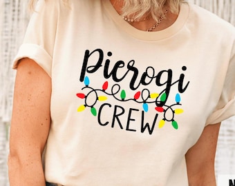 May include: A beige t-shirt with the text "Pierogi Crew" in black. The text is surrounded by a string of colorful Christmas lights.