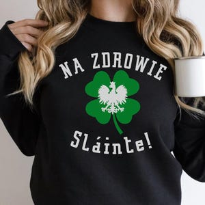May include: Black sweatshirt with a green four-leaf clover and a white eagle design. The text "NA ZDROWIE Sláinte!" is printed on the shirt.