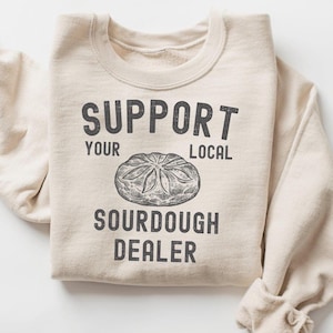 May include: A beige sweatshirt with the text "Support Your Local Sourdough Dealer" and a drawing of a sourdough loaf of bread.