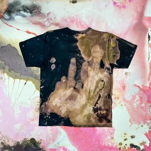 Op de afbeelding: Een zwart T-shirt met een bruin en zwart tie-dye patroon. Het patroon lijkt op een handafdruk.