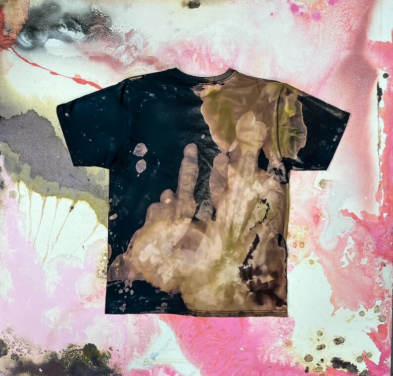 Op de afbeelding: Een zwart T-shirt met een bruin en zwart tie-dye patroon. Het patroon lijkt op een handafdruk.