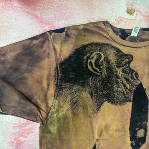 May include: A brown t-shirt with a black and white image of a chimpanzee's face on the front.