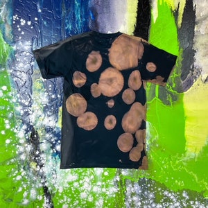 May include: A black t-shirt with a bleach-splattered design. The design features a pattern of irregular circles in shades of brown.