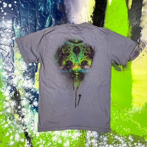 May include: A gray t-shirt with a colorful graphic print of a psychedelic design with green, blue, and black colors. The design has a dripping effect.