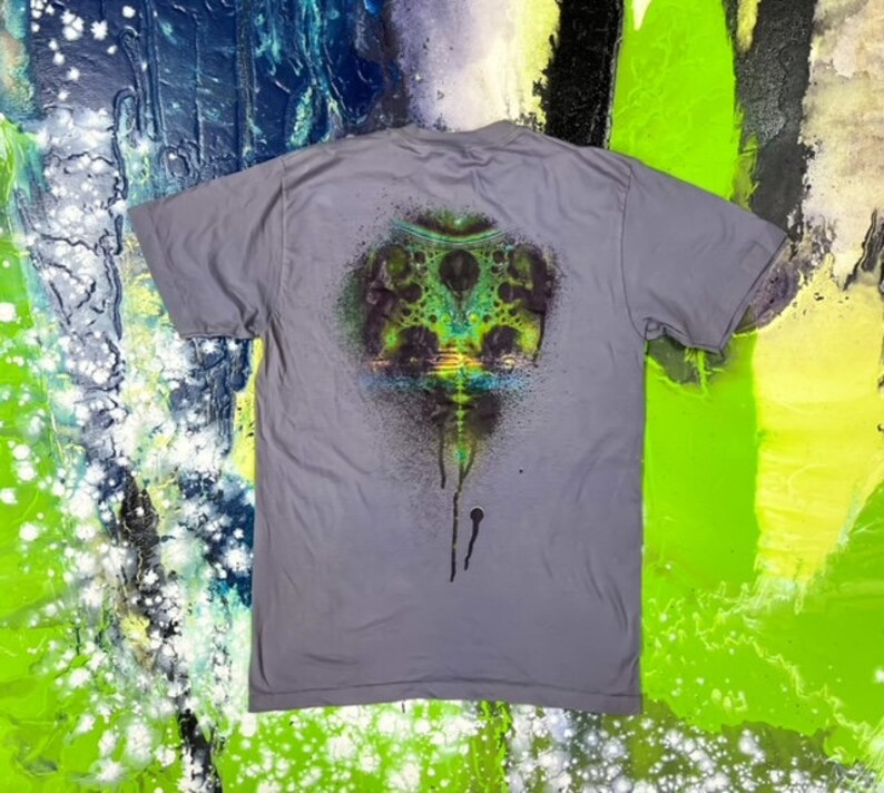 May include: A gray t-shirt with a colorful graphic print of a psychedelic design with green, blue, and black colors. The design has a dripping effect.