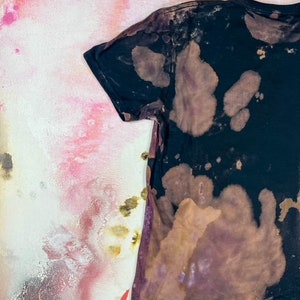 K&ouml;nnte beinhalten: Ein schwarzes T-Shirt mit einem braunen und wei&szlig;en Batik-Muster. Das Shirt hat einen Used-Look und ist aus einem weichen, bequemen Stoff.