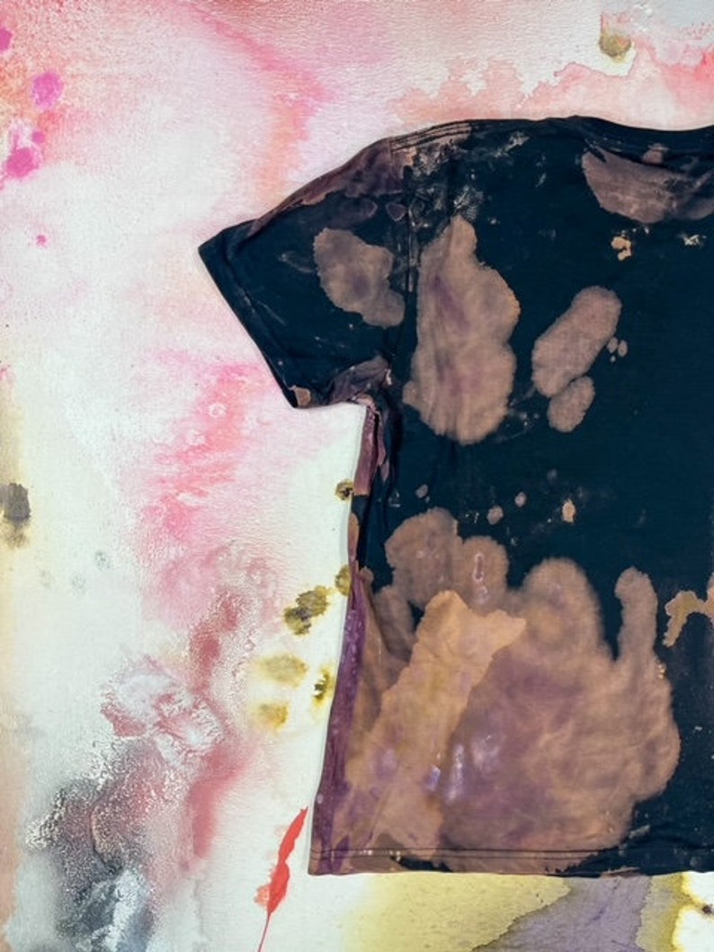 K&ouml;nnte beinhalten: Ein schwarzes T-Shirt mit einem braunen und wei&szlig;en Batik-Muster. Das Shirt hat einen Used-Look und ist aus einem weichen, bequemen Stoff.