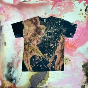 May include: A black t-shirt with a bleach-splattered design. The design features a white, abstract pattern with a brown and green splatter effect.