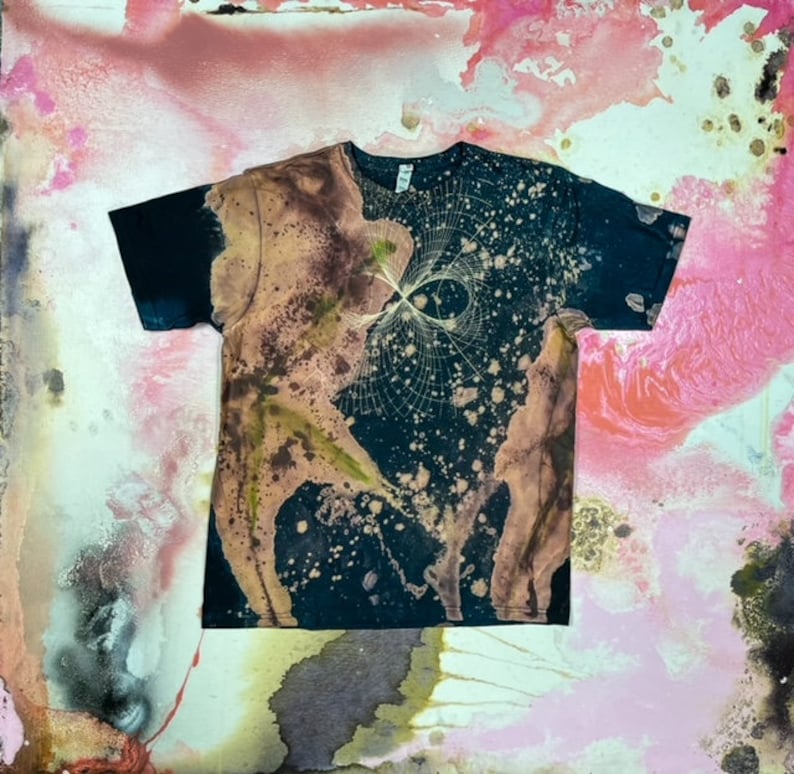 May include: A black t-shirt with a bleach-splattered design. The design features a white, abstract pattern with a brown and green splatter effect.