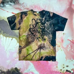 Op de afbeelding: Een zwart en groen tie-dye T-shirt met een zwarte octopus-grafische print. Het shirt heeft een verweerde look met een vervaagd, gespat design.