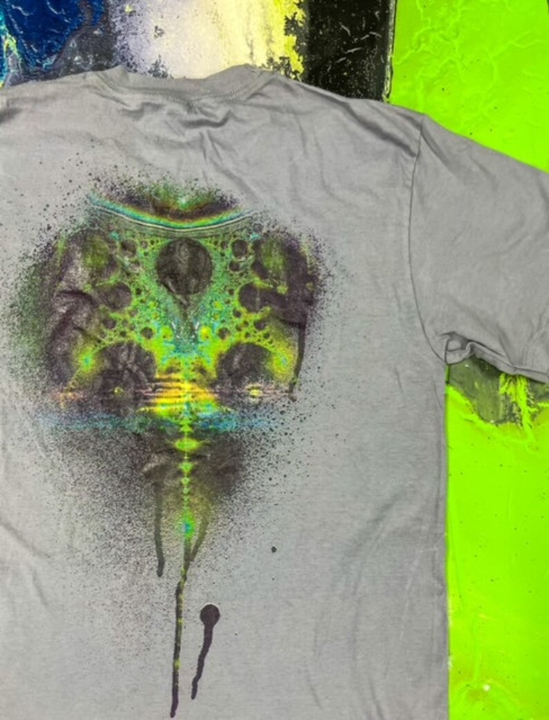 May include: Gray t-shirt with a green, blue, and black spray paint design of a swirling, abstract pattern.