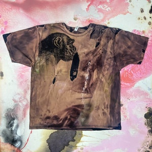 May include: A brown t-shirt with a faded image of a chimpanzee's face printed on the front. The shirt has a distressed look with a tie-dye effect.