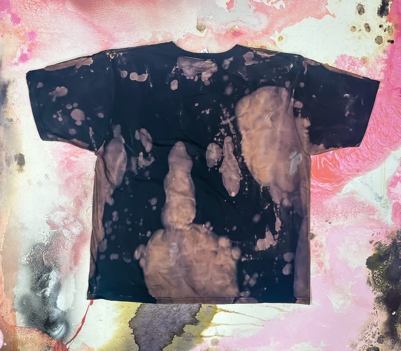 May include: A black t-shirt with a bleach-splattered design. The shirt has a distressed look with brown and white splotches.