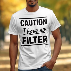 Könnte beinhalten: Weißes T-Shirt mit dem Text "CAUTION I have no FILTER" in fetten schwarzen Buchstaben. Das Shirt hat einen Rundhalsausschnitt und kurze Ärmel. Die Person auf dem Bild trägt eine blaue Jeans.