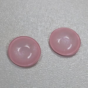 Op de afbeelding: Twee roze glazen schalen met een licht iriserende afwerking. De schalen zijn rond en hebben een ondiepe, gebogen vorm.
