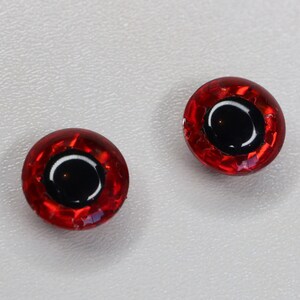 Peut inclure: Deux yeux de bricolage ronds et rouges avec des pupilles noires et une surface facettée réfléchissante. Ces yeux en plastique sont conçus pour être utilisés dans divers projets de bricolage, tels que la fabrication de poupées, de jouets ou d'autres articles faits à la main.