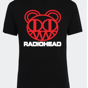 May include: Black t-shirt with a red bear-like graphic and the white text "RADIOHEAD". The graphic has circular ears, "DD" eyes, and a jagged mouth. A crew neck tee, a staple for casual wear.