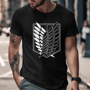May include: A black short-sleeved t-shirt featuring a large white graphic print on the chest. The design displays the Wings of Freedom emblem, which consists of two overlapping shield-shaped wings outlined in white against a solid black background.