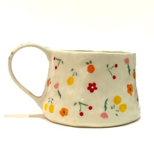 May include: A white ceramic mug with a textured surface and a floral pattern in shades of red, orange, yellow, and green.