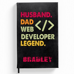 Puede incluir: Cuaderno de cuero negro con el texto "Husband. Dad <> Web Developer Legend." y el nombre "Bradley" en rojo.