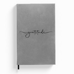 Puede incluir: Diario de imitaci&oacute;n de cuero gris con la palabra "gratitud" escrita en cursiva en la portada.