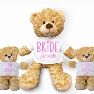 May include: Five plush teddy bears wearing white t-shirts with pink text. One bear has a "BRIDE" shirt with the name "Amanda" and the other four bears have "I DO CREW" shirts with different names.
