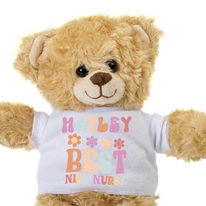 May include: A light brown teddy bear wearing a white t-shirt with the text "Hayley Best NIC Nurse" in colorful letters and flowers.