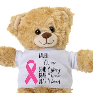 May include: A brown teddy bear wearing a white t-shirt with a pink ribbon and the text "LAURIE YOU are BEAR-Y strong BEAR-Y brave BEAR-Y loved"