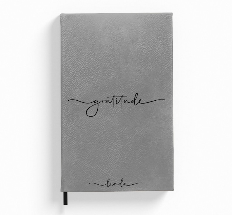 Puede incluir: Diario de imitaci&oacute;n de cuero gris con la palabra "gratitud" escrita en cursiva y el nombre "linda" escrito en cursiva en la parte inferior.
